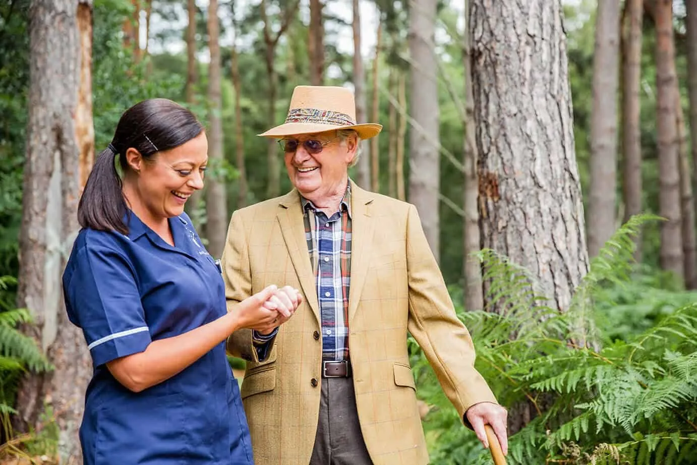 A resident and a carer walking together in the woodland at Kings Lodge, Camberley